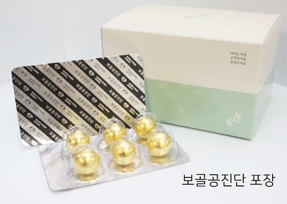 흰색과 연두색 상자 앞에 금색 환약이 담긴 블리스터 팩과 은색 포장지가 놓여 있다.