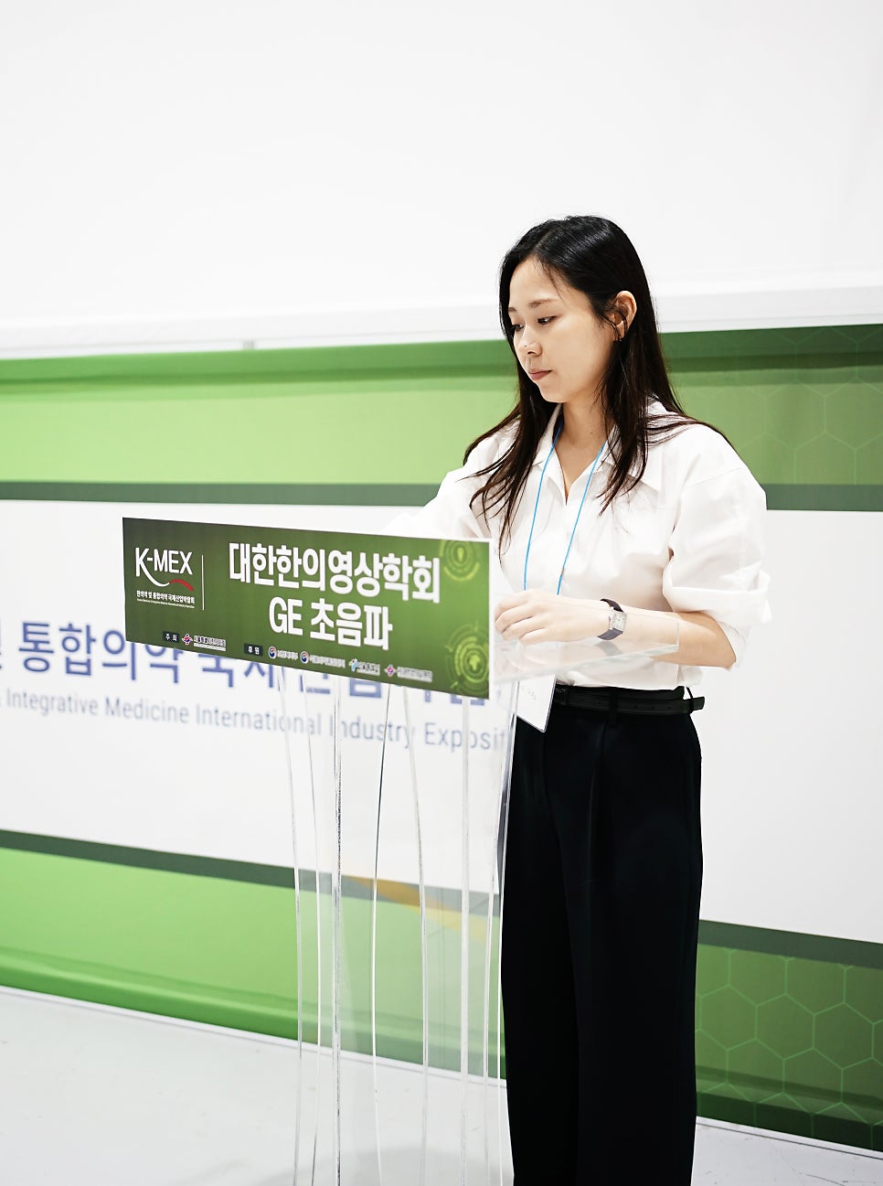 한 여성이 연단 뒤에서 발표 자료를 보고 있다.