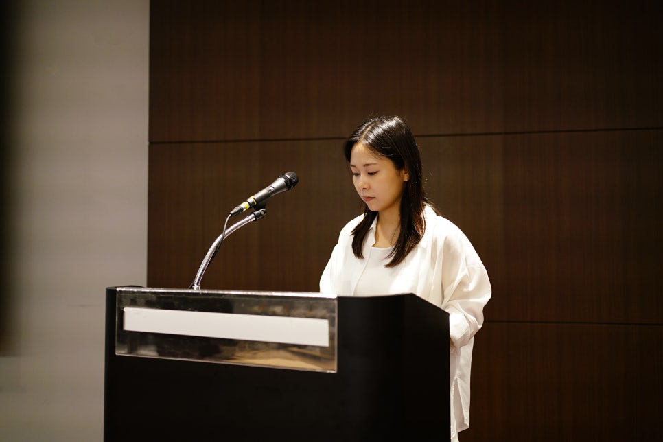 마이크가 있는 검은색 연단 뒤에 서서 아래를 보고 있는 여성
