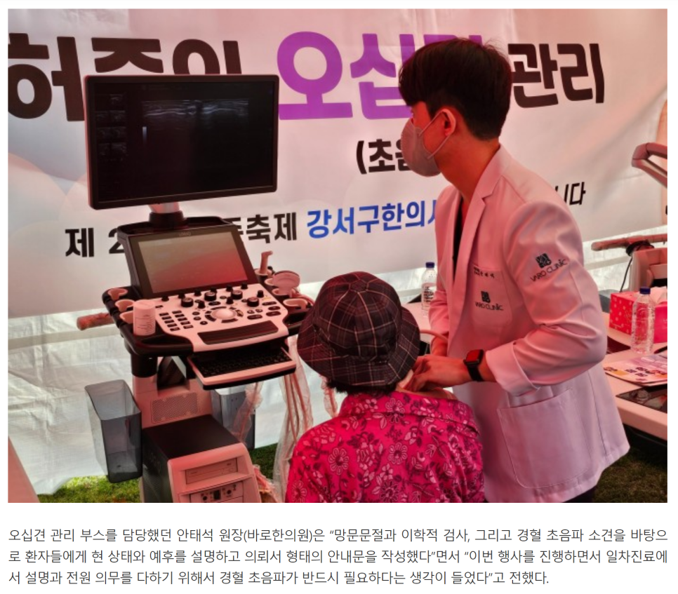 한의사가 축제 부스에서 환자의 목 부위에 초음파 검사를 하고 있으며, 초음파 화면이 보인다.