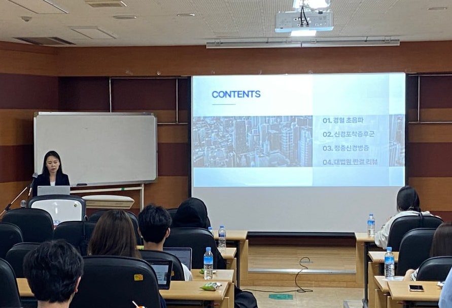 강의실에서 발표자가 '경혈 초음파'가 포함된 목차 슬라이드를 보여주며 강연하고 있다.