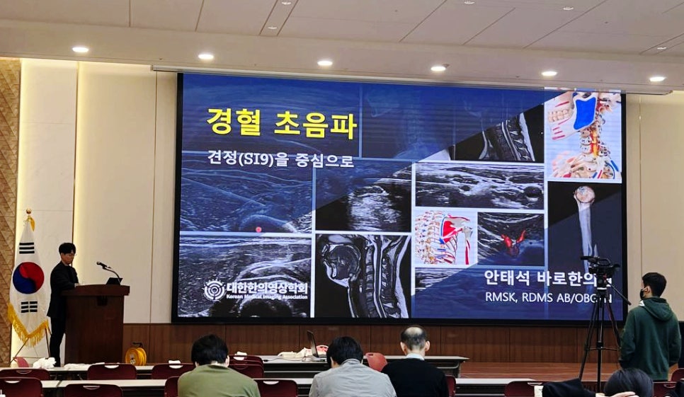 강당에서 한의사가 '경혈 초음파'를 주제로 발표하고 있으며, 스크린에는 초음파 영상과 해부학적 그림 등 다양한 의료 영상이 표시되어 있다.