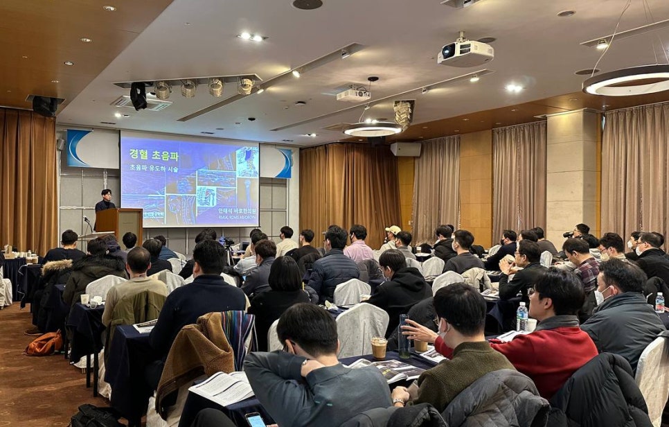 강사가 연단에서 경혈 초음파 관련 내용을 발표하고, 참석자들이 앉아서 듣고 있는 강의실 풍경.