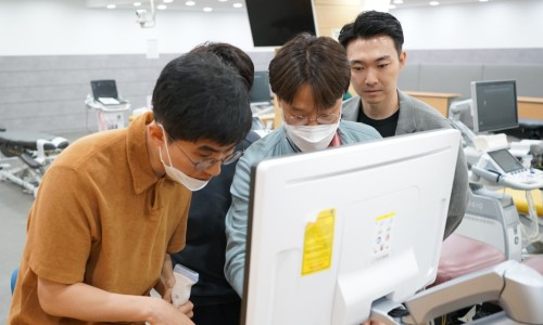 여러 명이 초음파 진단기기 모니터를 보며 실습 교육을 받고 있으며, 한 명이 초음파 탐촉자를 들고 있습니다.