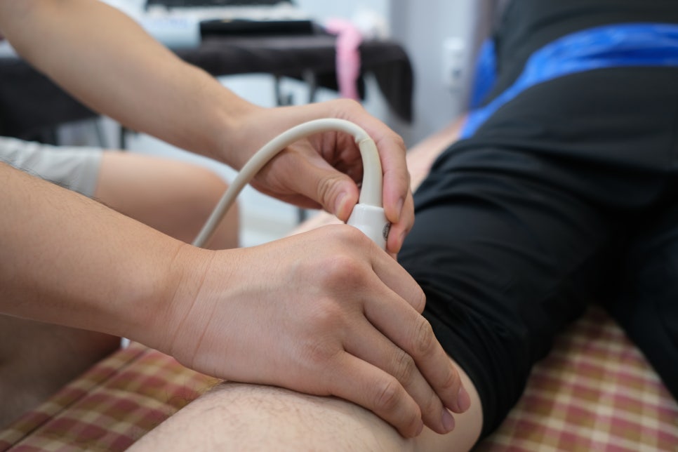 한 사람이 다른 사람의 다리에 초음파 탐촉자를 대고 있는 모습