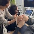 한 사람이 다른 사람의 목을 진찰하고 있으며, 뒤편에 초음파 기기가 놓여 있다.