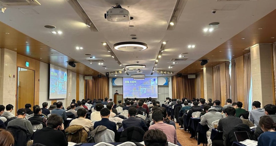 강당에서 많은 사람들이 강연을 듣고 있는 모습. 스크린에는 '경혈 초음파'라는 글자와 초음파 이미지가 보인다.