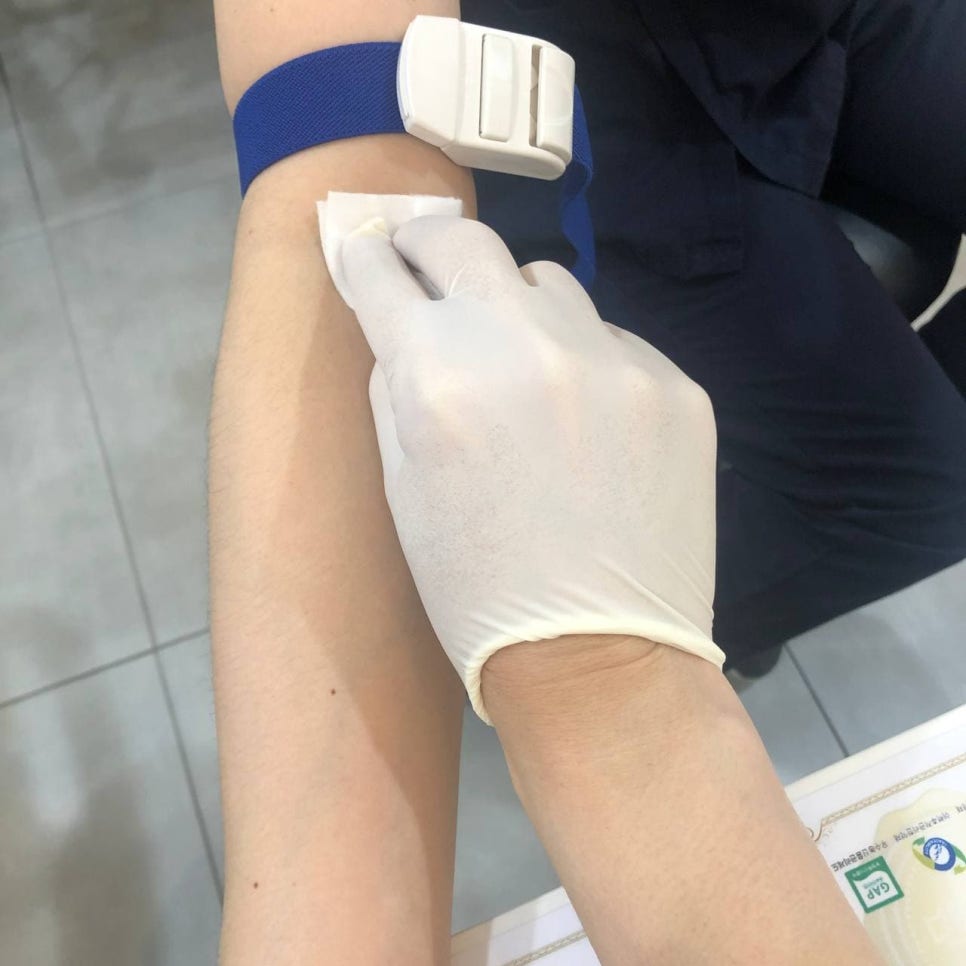 파란색 지혈대를 착용한 팔의 안쪽을 장갑 낀 손이 솜으로 닦고 있는 모습 — 서울 바로한의원 초음파 약침·도침