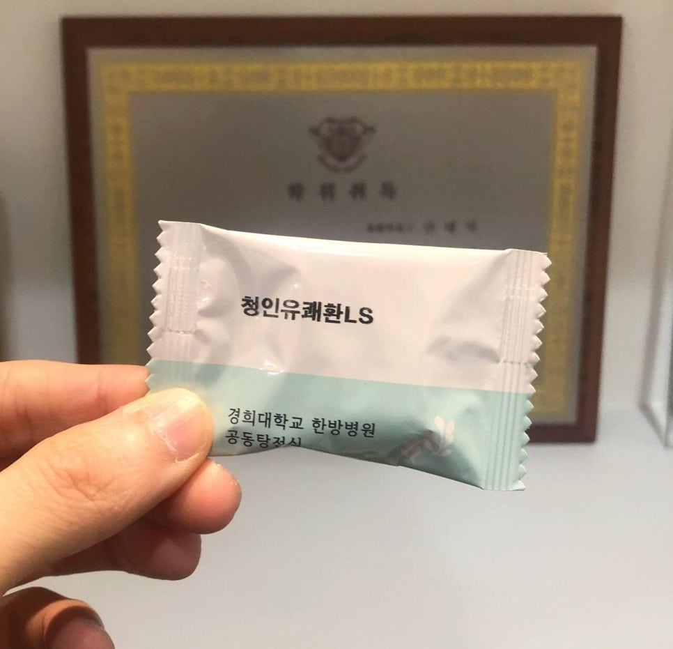 손이 '청인유쾌환LS'라고 적힌 흰색과 연두색 한약 포를 들고 있는 모습이다.