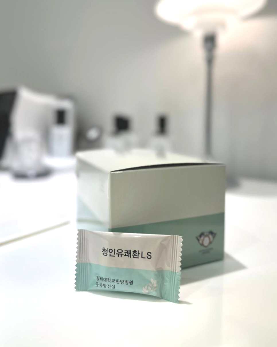 청인유쾌환 LS 개별 포장과 제품 상자가 흰색 테이블 위에 놓여 있으며, 포장에는 '경희대학교 한방병원 공동탕전실' 문구가 보인다.