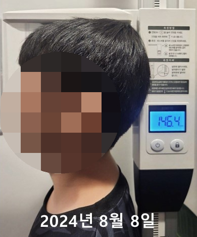 키 측정 기계에 서 있는 아이의 옆모습과 146.4로 표시된 측정값