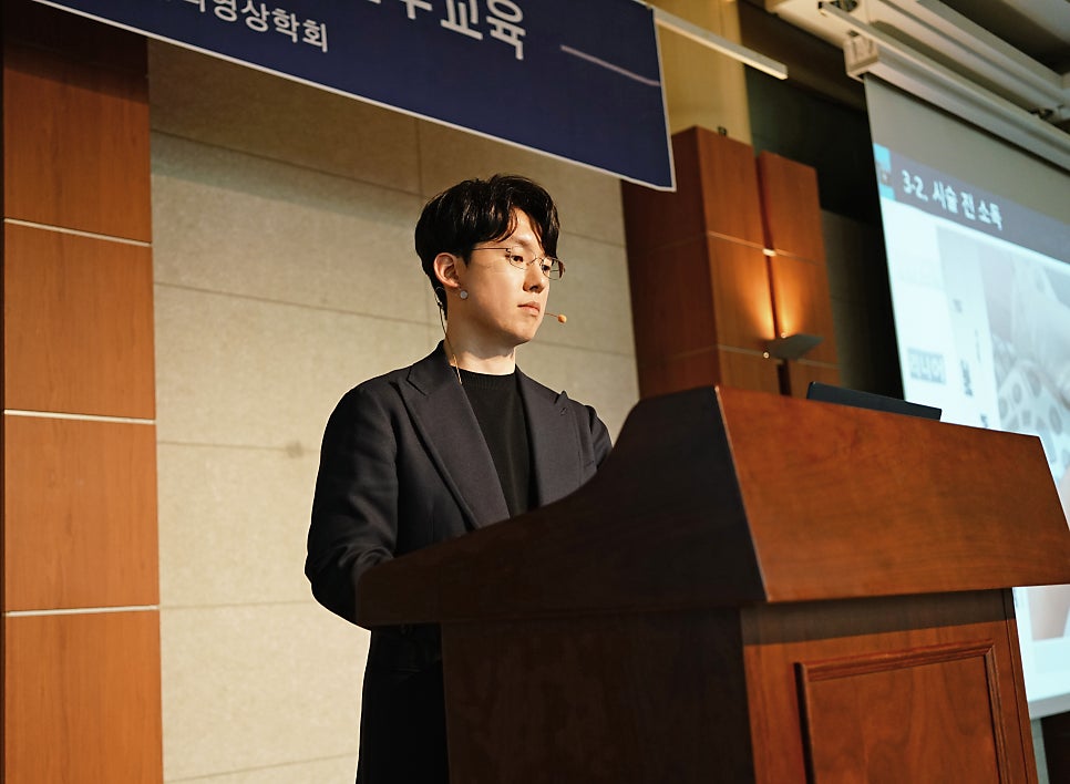 안경을 쓴 남성이 강단에서 마이크를 착용하고 발표하고 있다.