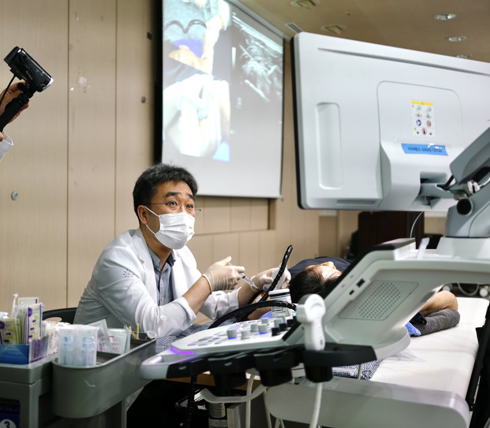 마스크를 쓴 남성 의사가 초음파 기기를 보며 환자에게 시술하고 있다.