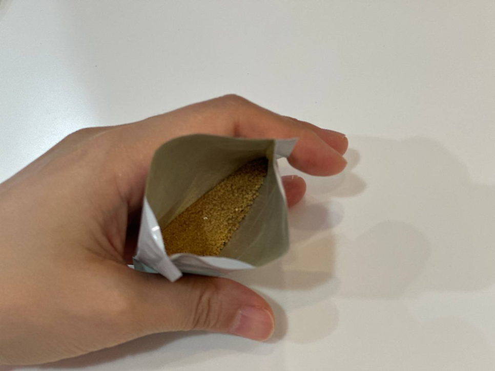 손이 열린 파우치를 들고 있으며, 파우치 안에 갈색 가루가 담겨 있습니다.