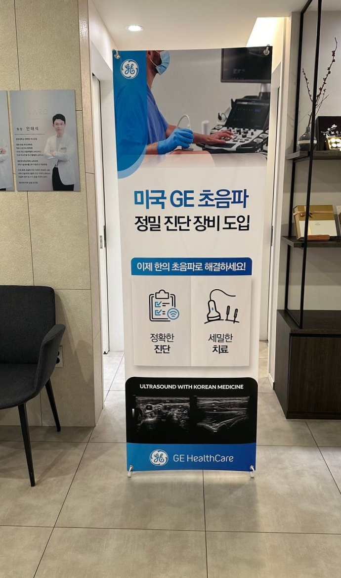 한의원 내부에 설치된 GE 초음파 장비 도입 안내 배너로, 초음파 기기를 조작하는 사람과 초음파 영상이 함께 인쇄되어 있다 — 초음파 정밀 진단 | 서울 바로한의원 초음파 약침·도침·침도