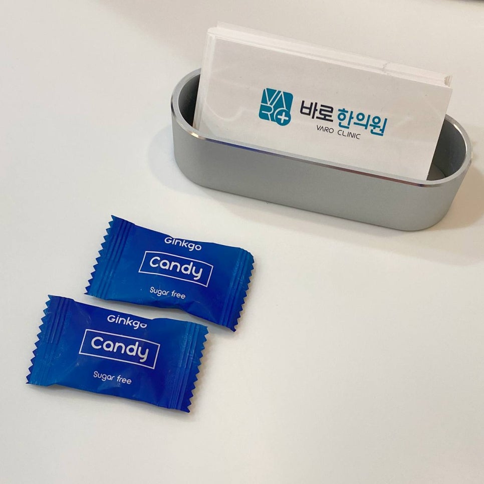 흰색 테이블 위에 파란색 징코 캔디 두 개와 바로 한의원 명함꽂이가 놓여 있다.