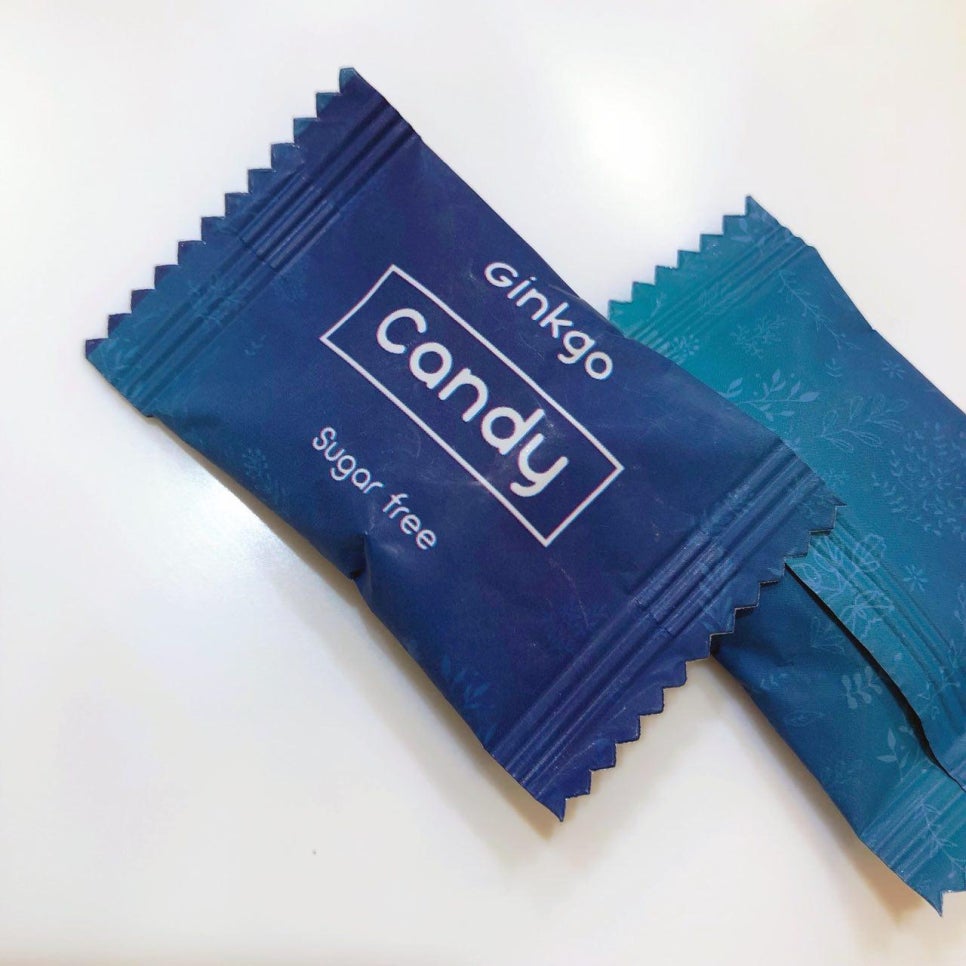 흰색 배경에 놓인 두 개의 개별 포장된 캔디. 앞쪽 캔디 포장지에는 'ginkgo Candy Sugar free'라고 쓰여 있다.