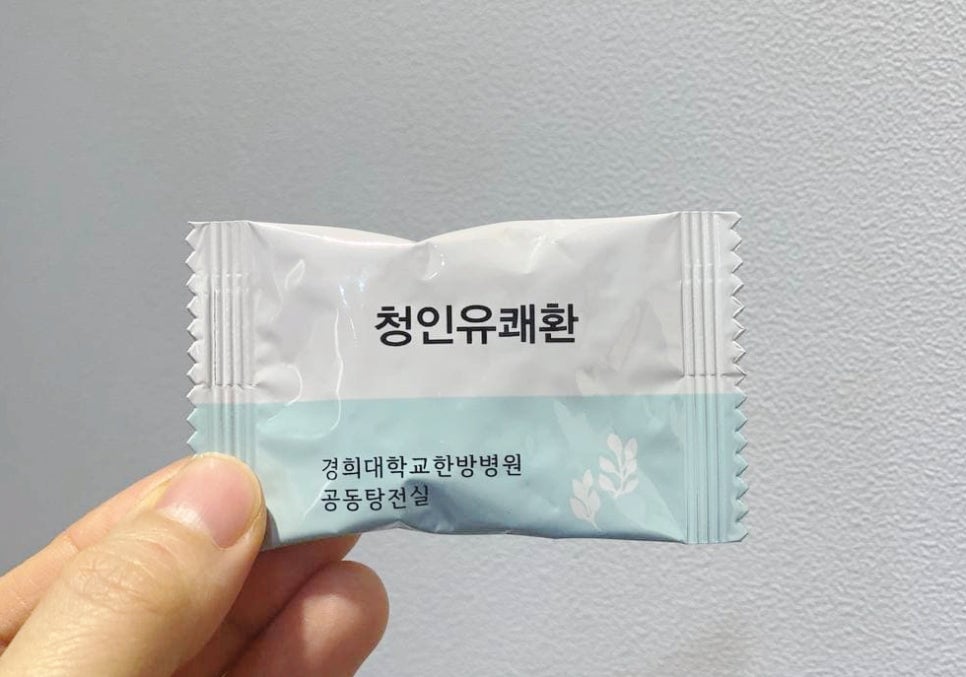 손이 '청인유쾌환'과 '경희대학교한방병원 공동탕전실'이라고 적힌 흰색과 하늘색 포장지를 들고 있는 모습.