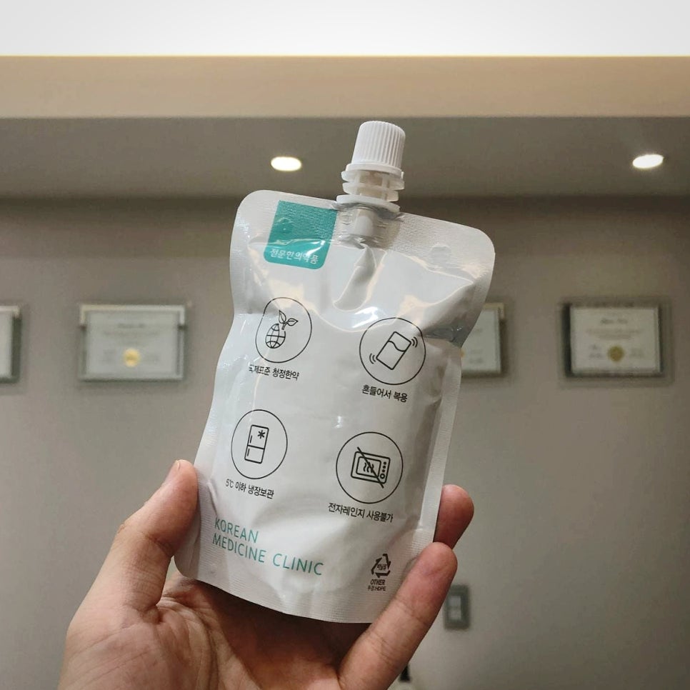 손이 'KOREAN MEDICINE CLINIC'이라고 적힌 흰색 파우치를 들고 있다.