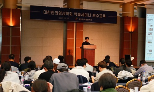 강사가 연단에서 발표하고 있으며, 청중들이 앉아 세미나를 듣고 있는 모습