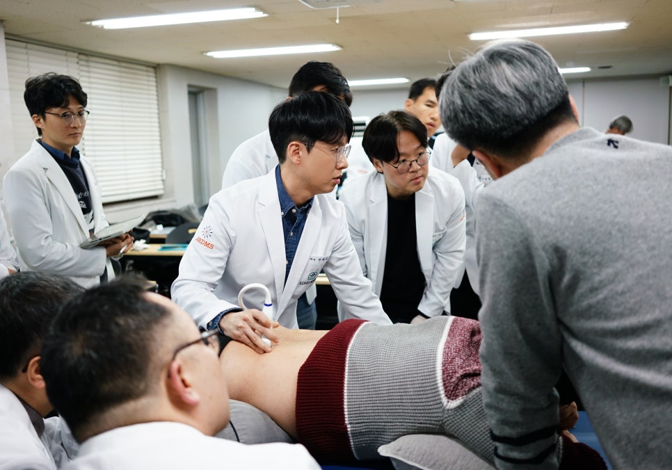 흰 가운을 입은 사람들이 누워있는 사람의 등에 초음파 기기를 사용하는 모습을 보고 있다 — 초음파 정밀 진단 | 서울 바로한의원 초음파 약침·도침·침도