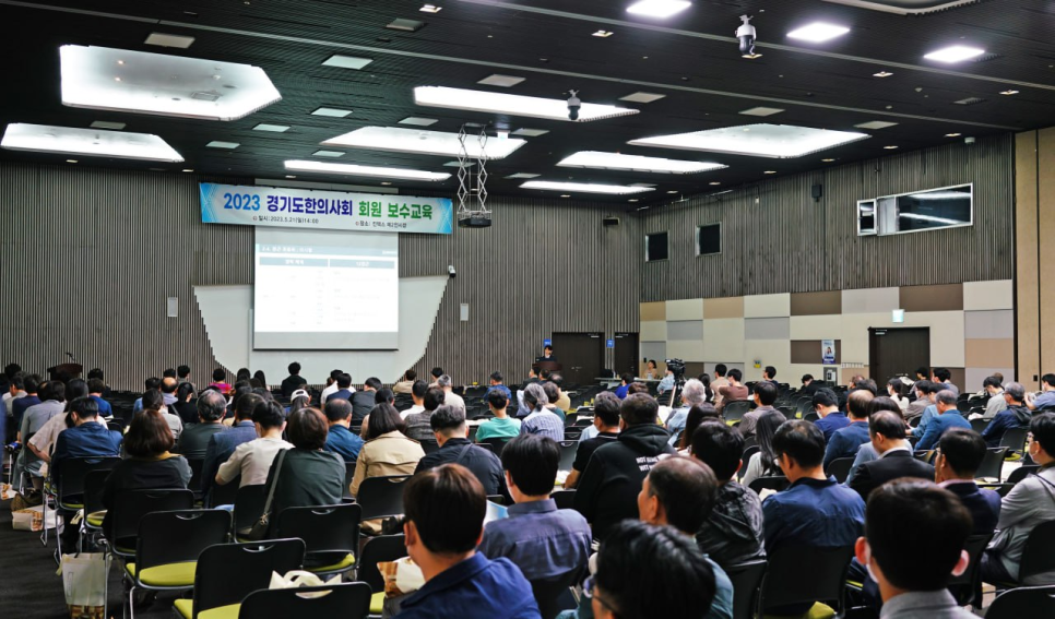 강당에 앉아 스크린을 바라보는 많은 사람들의 모습으로, 스크린에는 '2023 경기도한의사회 회원 보수교육'이라는 글자가 보인다.