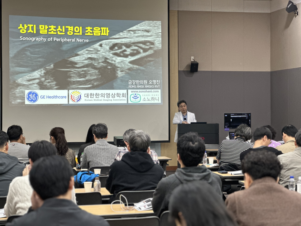 학회에서 한의사가 상지 말초신경 초음파에 대해 발표하고 있으며, 스크린에 초음파 영상과 발표 제목이 보입니다.