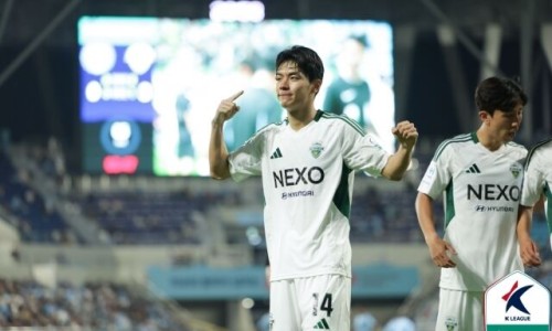 K리그 경기장에서 흰색 유니폼을 입은 전진우 선수가 손가락으로 머리를 가리키고 있다 — 서울 바로한의원 초음파 약침·도침