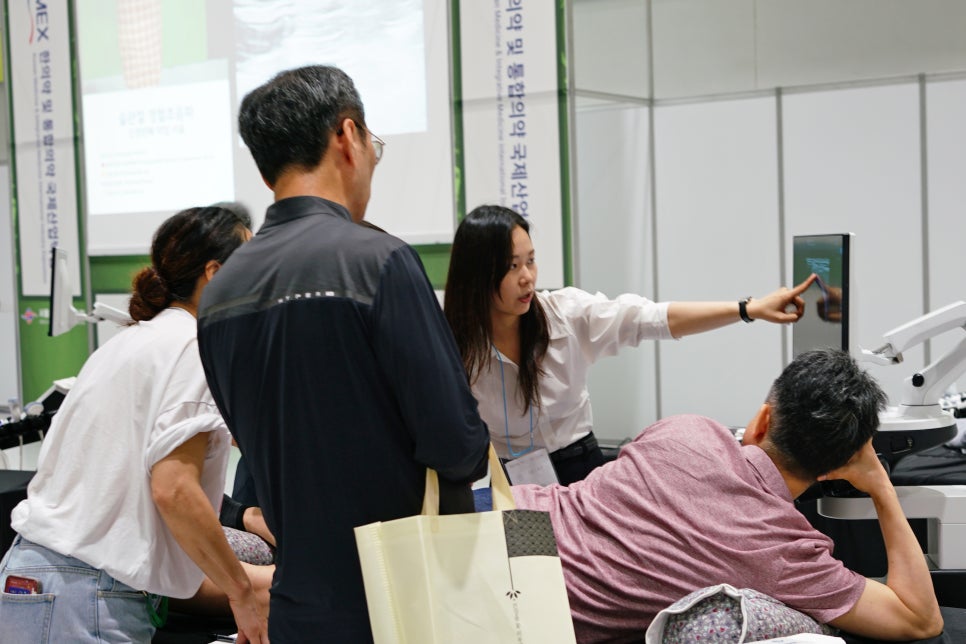 한 여성이 초음파 기기 화면을 가리키며 설명하고 있고, 여러 사람이 이를 지켜보고 있다.