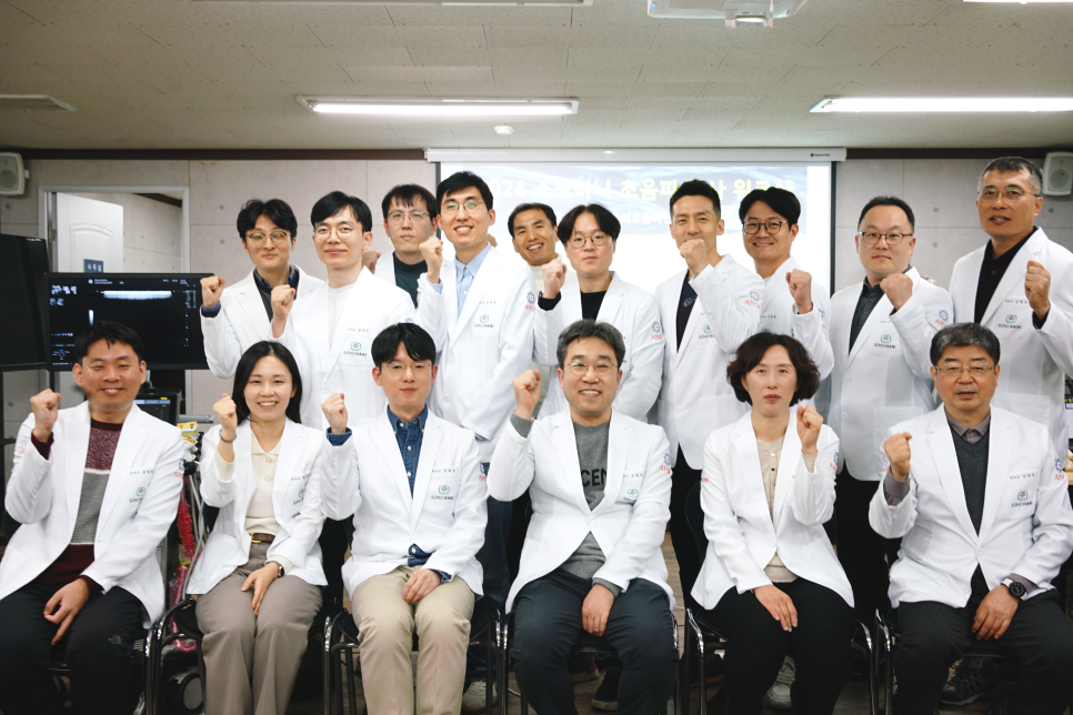 흰색 가운을 입은 여러 명의 사람들이 주먹을 쥐고 웃으며 포즈를 취하고 있다. 배경에는 프로젝터 화면과 초음파 모니터가 보인다 — 초음파 정밀 진단 | 서울 바로한의원 초음파 약침·도침·침도