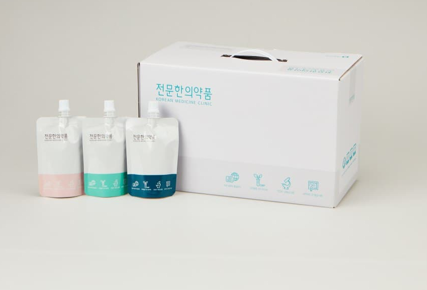 세 가지 색상의 파우치 한약과 흰색 상자가 함께 놓여 있는 모습