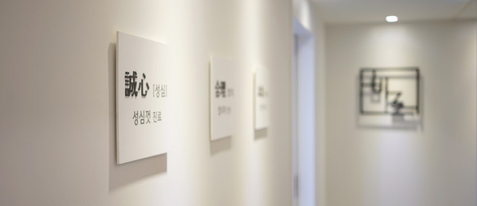 하얀 벽에 '誠心 [성심] 성심껏 진료'라고 쓰인 표지판이 걸려 있는 한의원 복도 — 서울 바로한의원 초음파 약침·도침