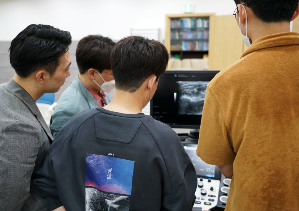 여러 사람이 초음파 모니터를 보며 화면 속 초음파 영상을 관찰하고 있다.