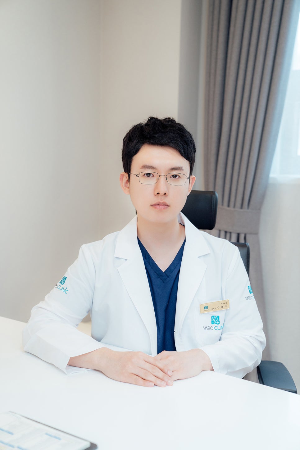 안경을 쓴 남자 한의사가 흰색 가운을 입고 책상에 앉아 정면을 바라보고 있다 — 서울 바로한의원 초음파 약침·도침