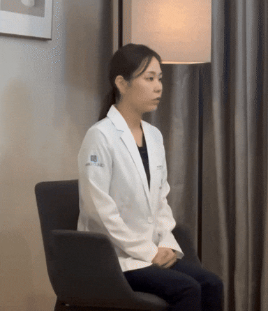 하얀 가운을 입은 여성이 의자에 앉아 옆을 보고 있습니다.