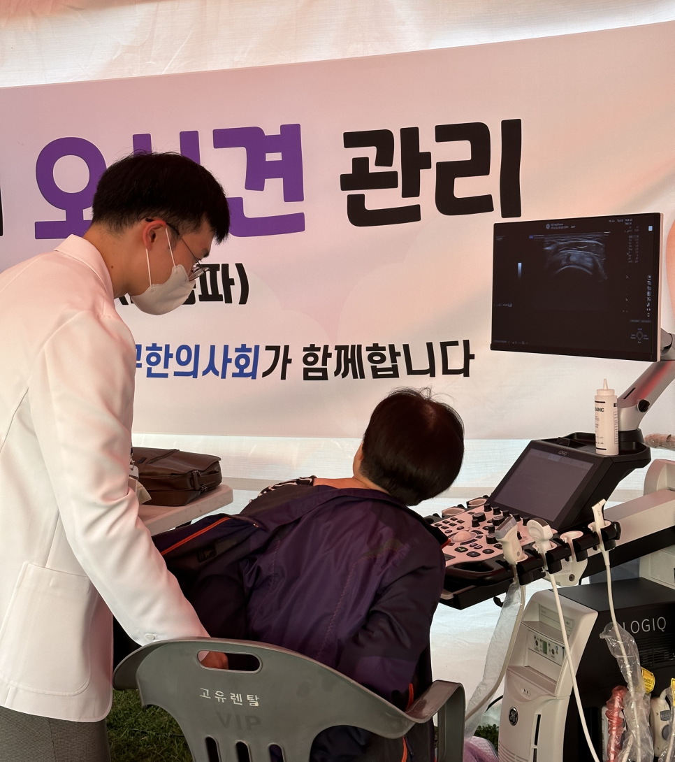 야외 부스에서 한의사가 환자의 등에 초음파 검사를 하는 모습과 초음파 화면.