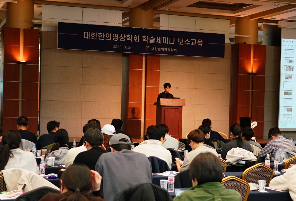 강사가 연단에서 발표하고 여러 참석자가 앉아 경청하는 학술 세미나 풍경