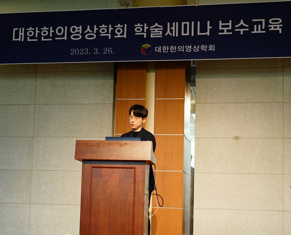 한 남성이 강단에 서서 발표하고 있으며, 뒤편에는 '대한한의영상의학회 학술세미나 보수교육'이라고 적힌 현수막이 걸려 있다.