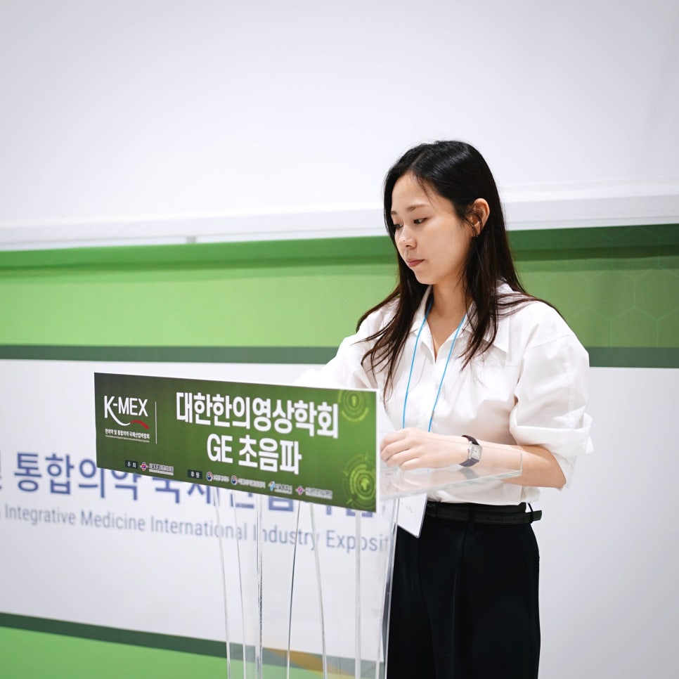 대한한의영상의학회와 GE 초음파 로고가 있는 연단 뒤에 서 있는 여성