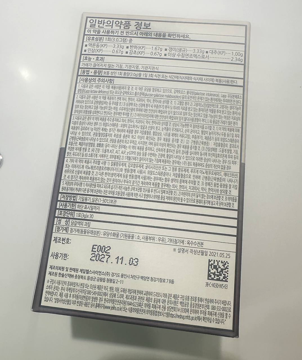 한약 제품의 일반의약품 정보가 적힌 흰색 라벨을 확대한 사진으로, 성분, 효능, 복용법, 주의사항, 유효기한 등이 상세히 표시되어 있다.