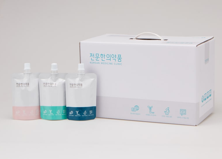 한의원 로고가 인쇄된 파우치 세 개와 흰색 상자가 흰 배경에 놓여 있다.