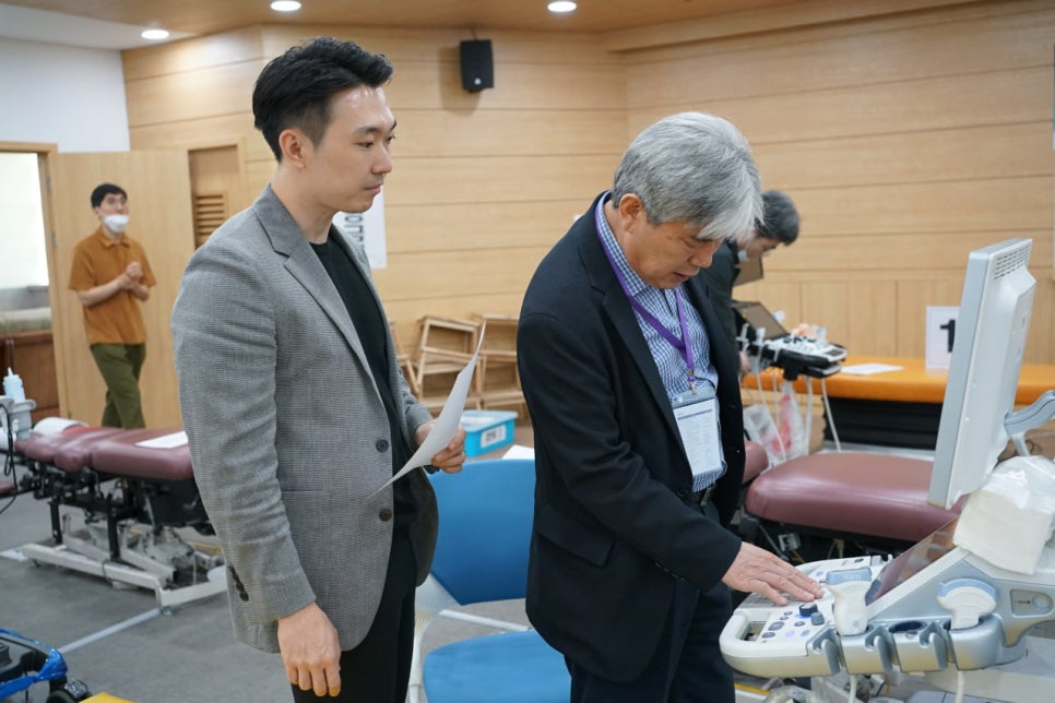 학술대회에서 한 남성이 초음파 기기를 조작하고 다른 남성이 옆에서 지켜보고 있다.