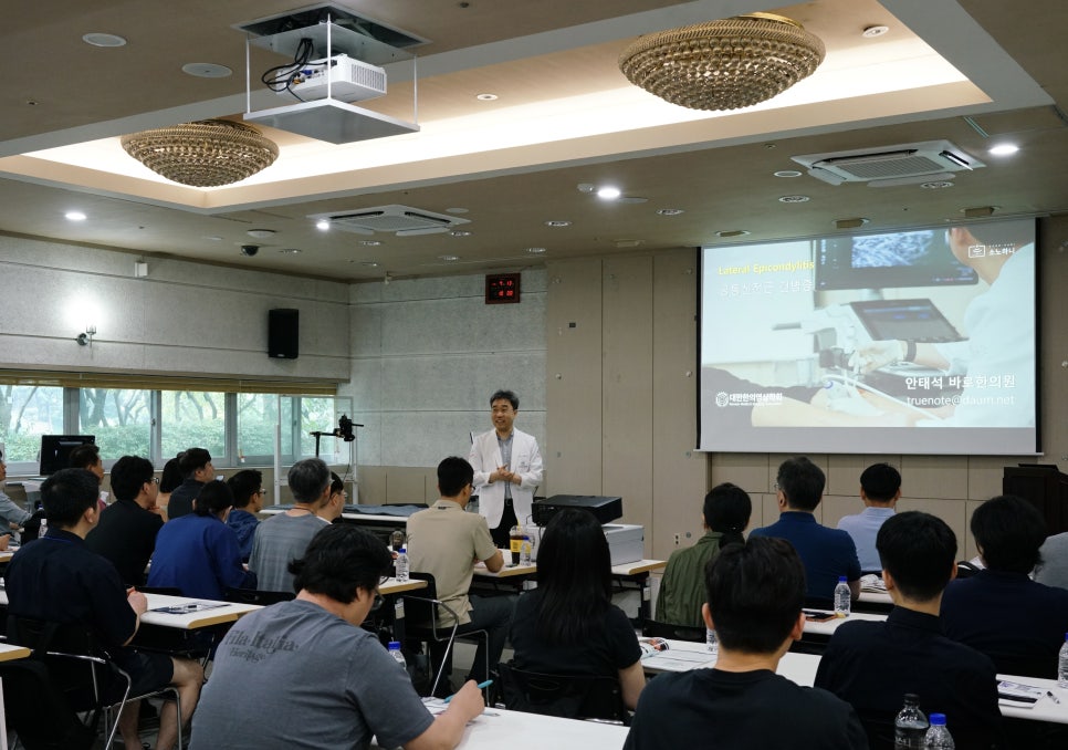 강사가 청중 앞에서 초음파 관련 강좌를 진행하고 있으며, 화면에는 초음파 영상이 보인다.