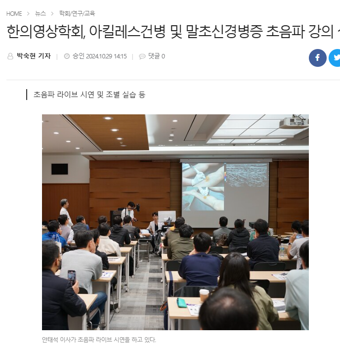강연장에서 강사가 화면에 초음파 시술 장면을 보여주며 라이브 시연을 하고 있으며, 여러 명의 수강생들이 이를 지켜보고 있다.