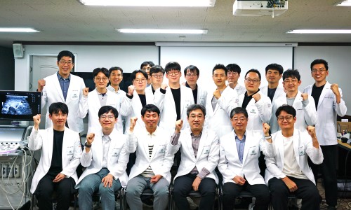 흰색 가운을 입은 남성들이 초음파 기기와 모니터가 있는 실내에서 주먹을 쥐고 포즈를 취하고 있다.