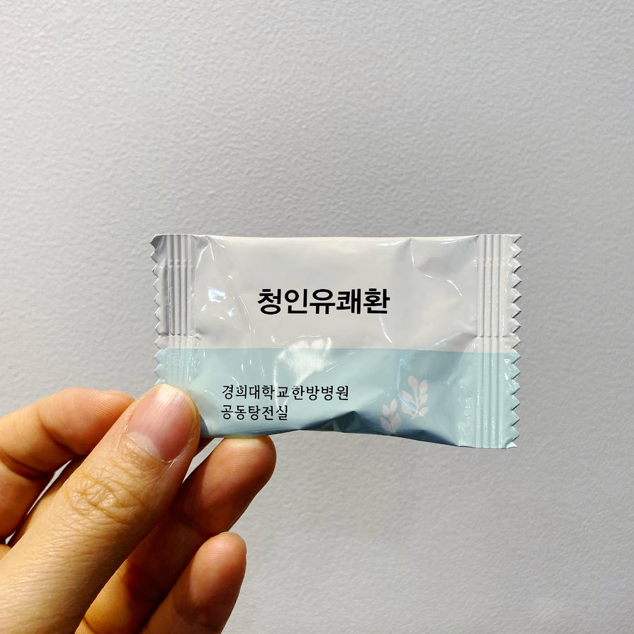 손이 경희대학교 한방병원 공동탕전실의 청인유쾌환이라고 쓰인 흰색과 하늘색 약 포장지를 들고 있는 모습.