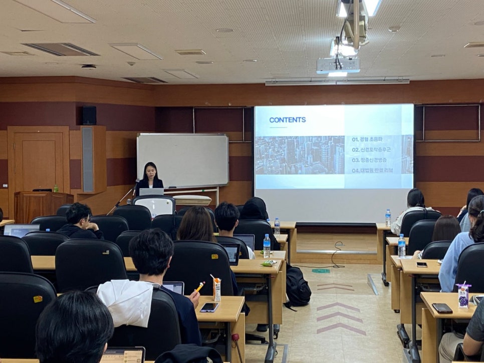 강의실에서 발표자가 강단에 서서 강연하고 있으며, 화면에는 '경혈 초음파'를 포함한 목차가 보인다.