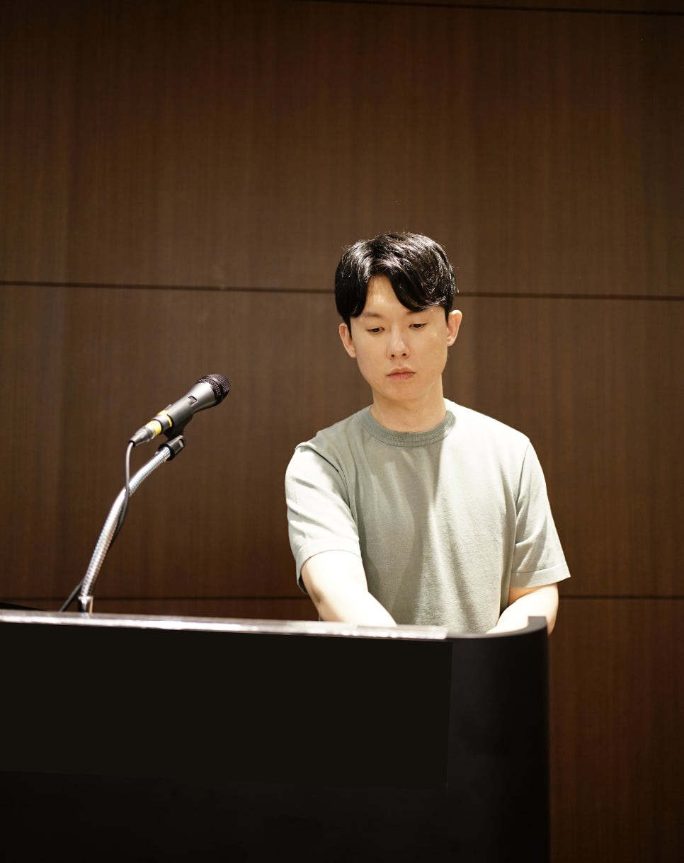 한 남성이 마이크 앞에 앉아 피아노를 연주하고 있다.
