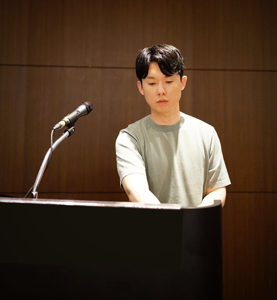 한 남자가 피아노를 연주하고 있으며, 왼쪽에 마이크가 놓여 있다.
