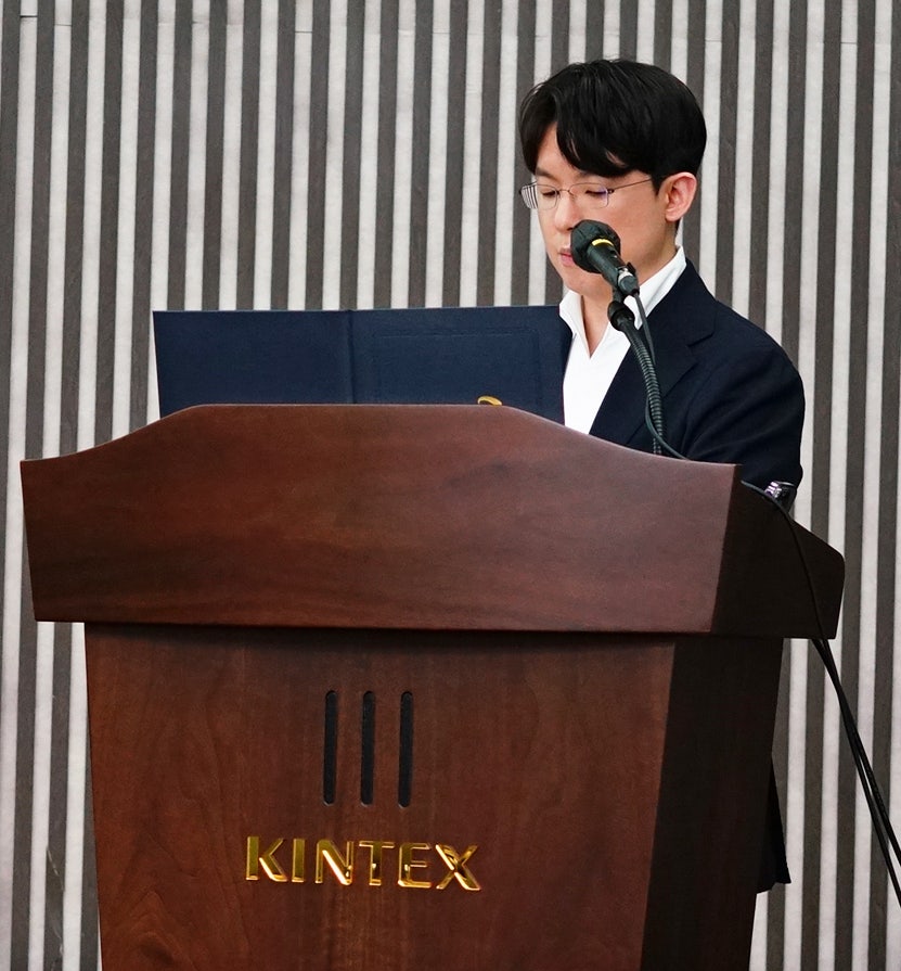 KINTEX 로고가 있는 연단에서 안경을 쓴 남성이 마이크 앞에서 발표하고 있다.